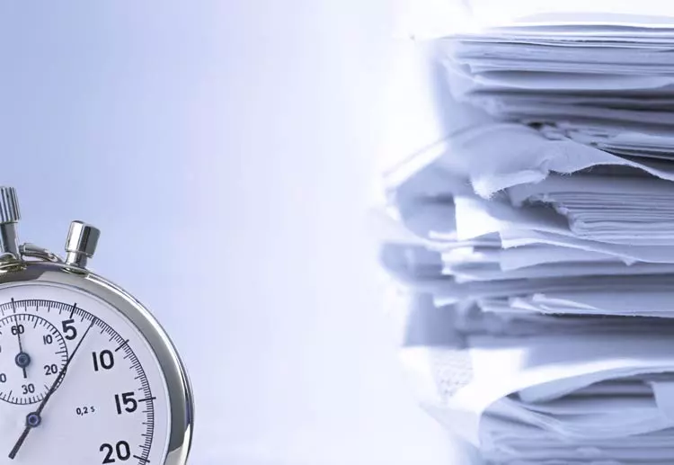 close de um relógio com uma pilha de papeis ao fundo - Por que digitalizar os documentos da sua empresa